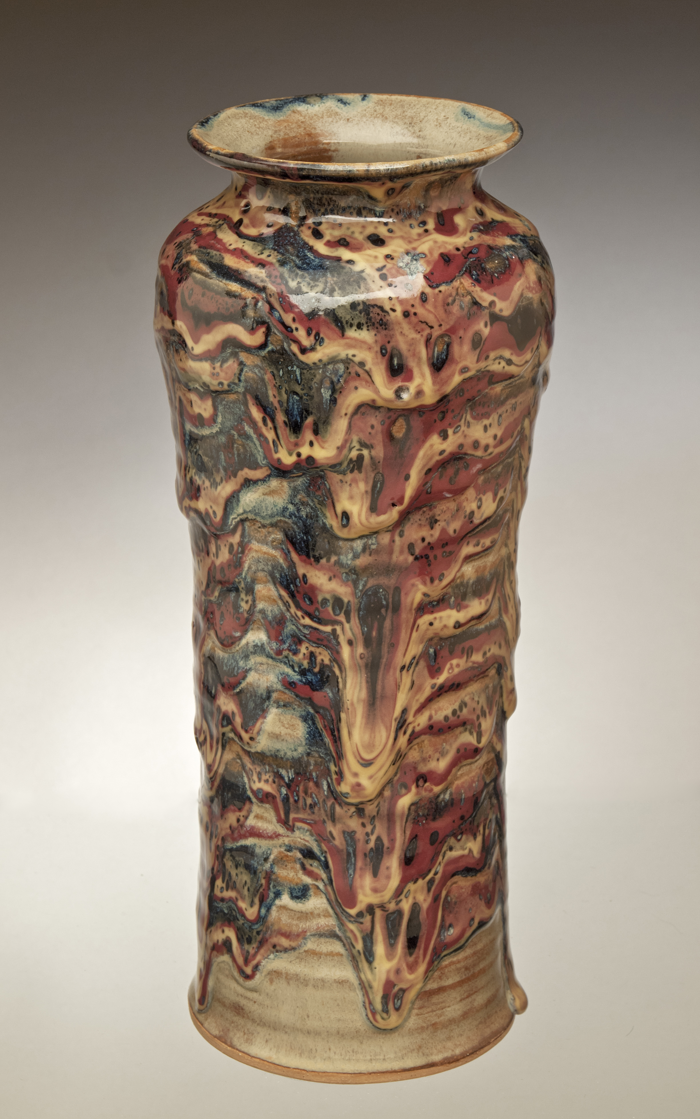 A tall, skinny vase with red, orange and black paint that appears to be dripping from the pot