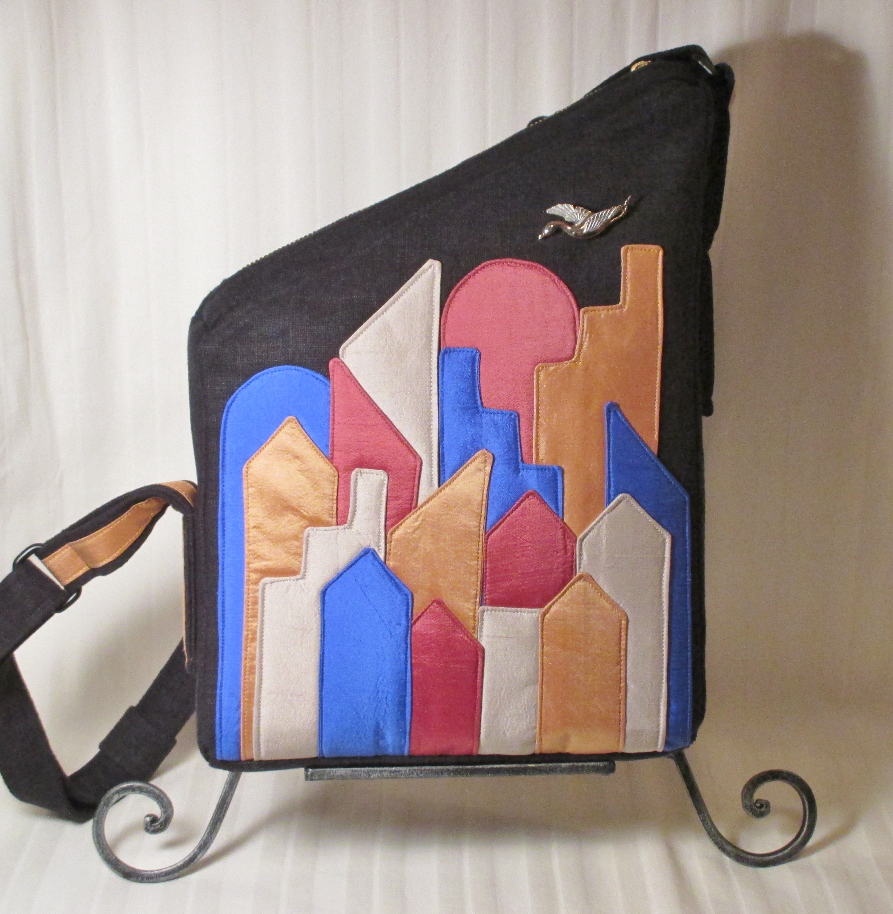 A black satchel with blue, tan abd pink silhouettes of buildings and a bird flying over