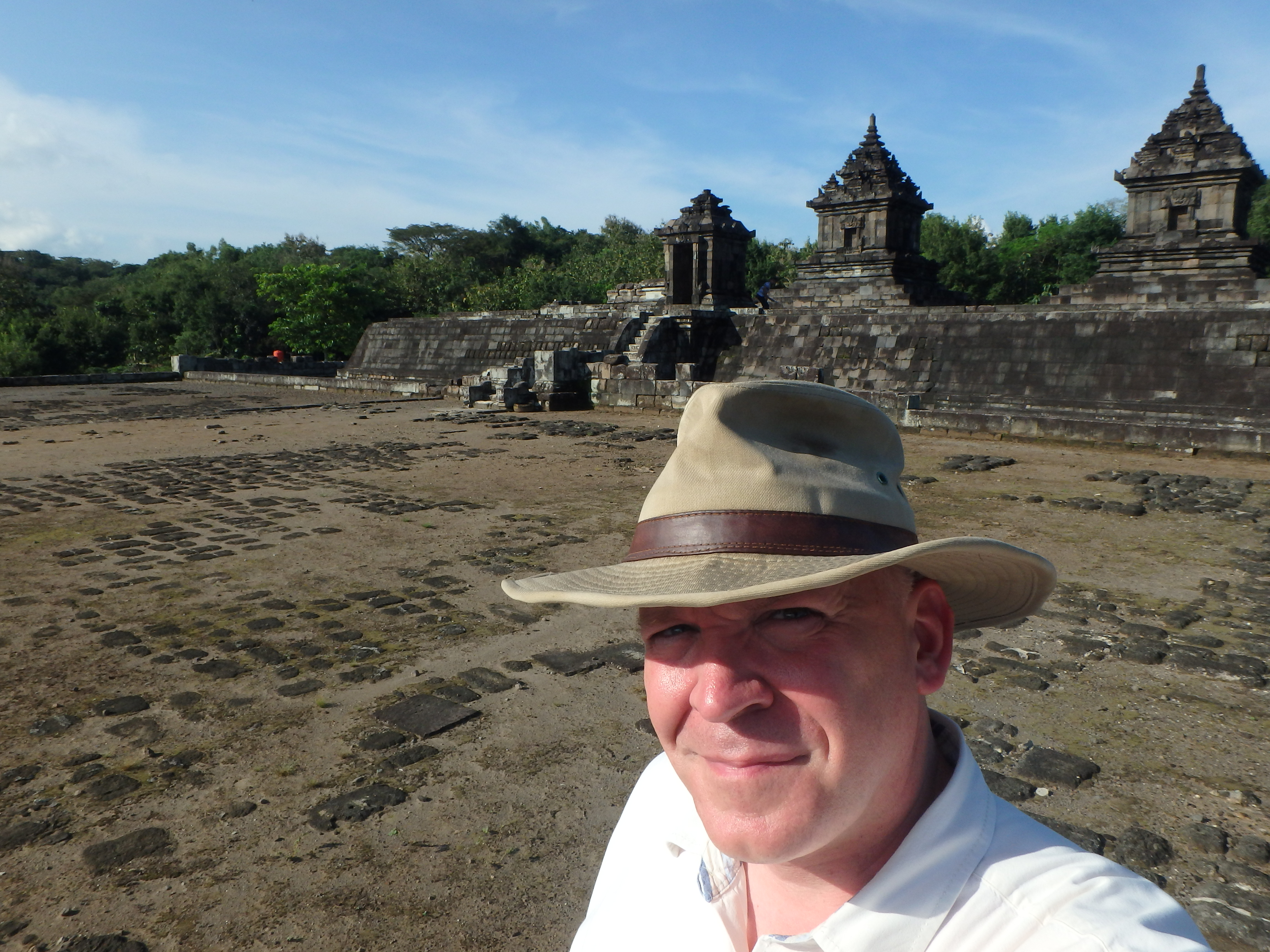 A self-taken photograph of a smiling wear wearing a hat and posing in front of ancient ruins