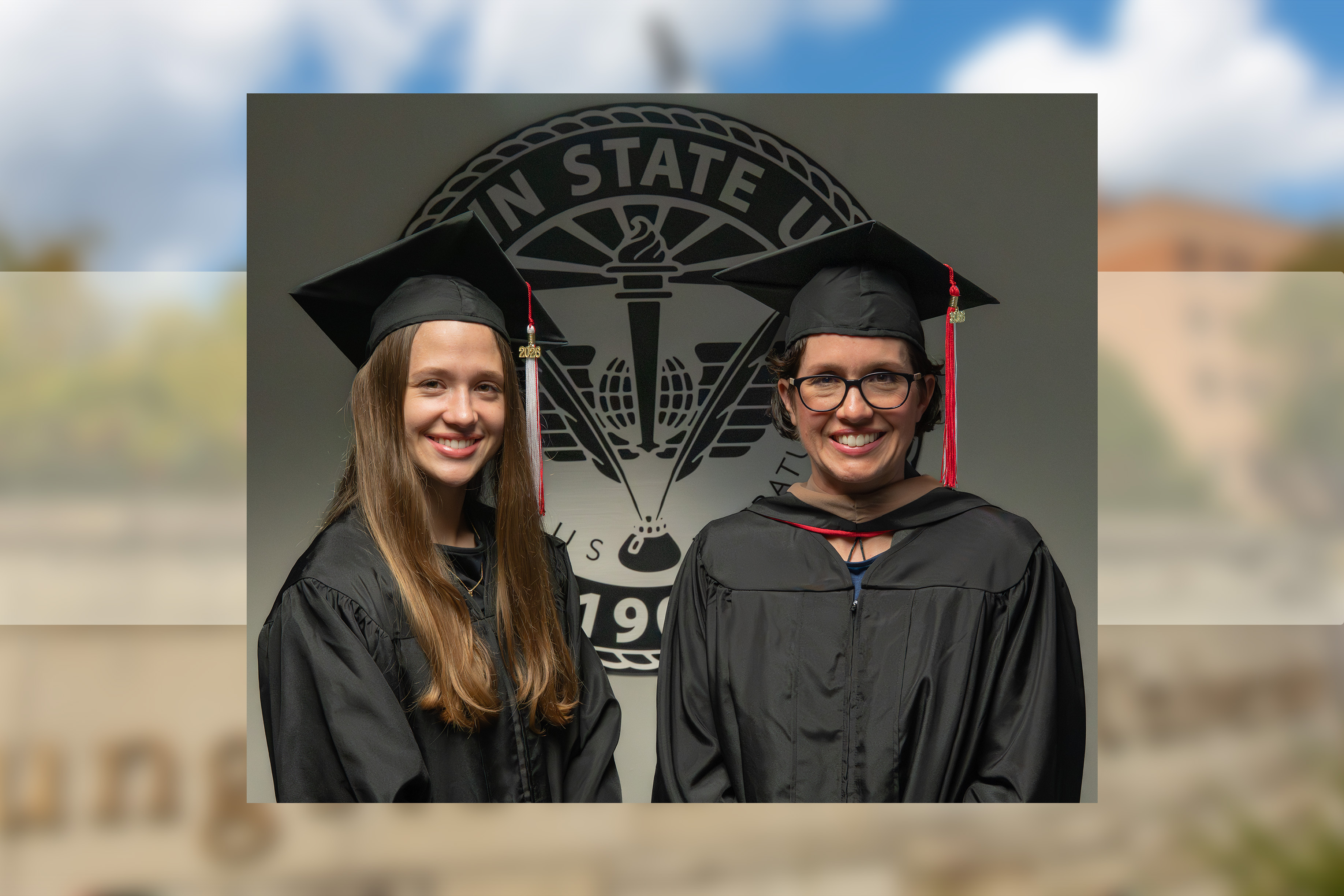 Olivia and Jennifer Jackson wearing their caps and gowns in front of the YSU seal