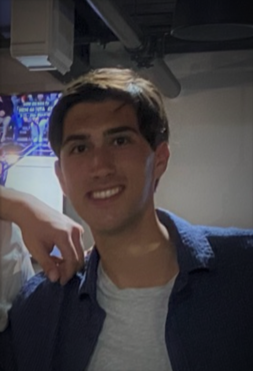 Anthony smiling wearing a white shirt with a blue collared button up over it