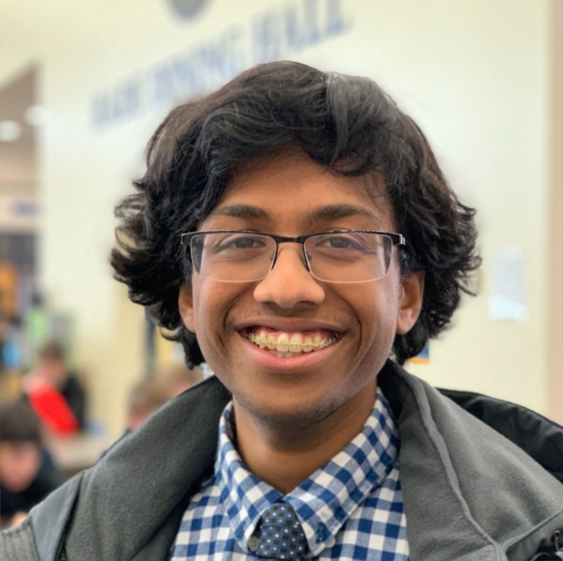 Sanat smiling and wearing a checkered shirt and tie