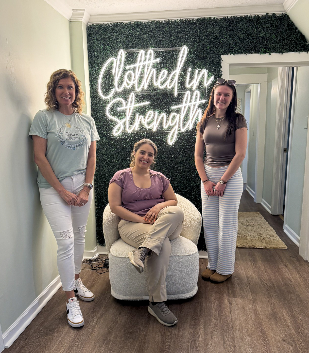 members of the Student Nonprofit Leadership Organization pose in front of the Clothed in Strength logo