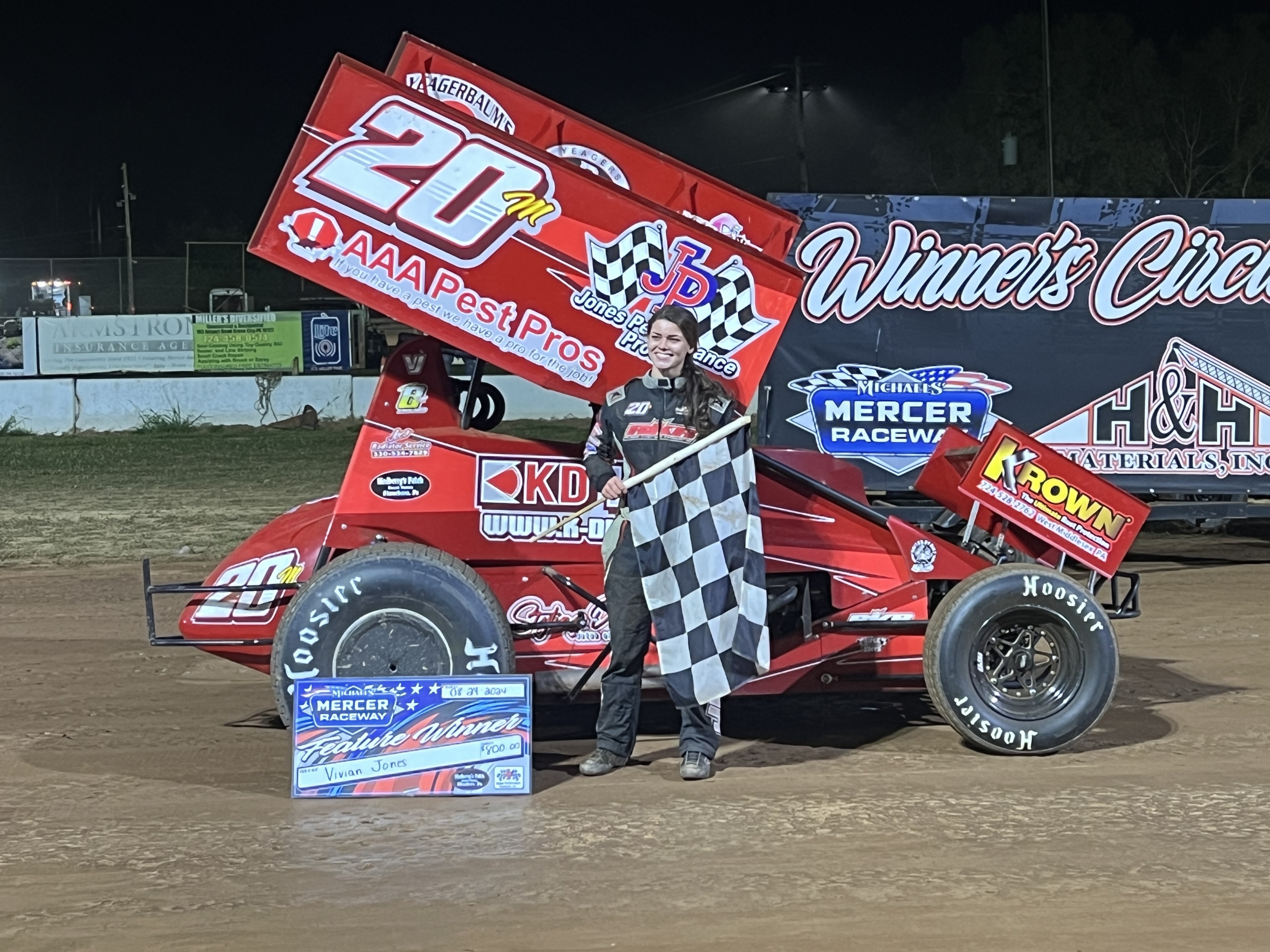 Vivian Jones with the checkered flag in front of her car on the racetrack