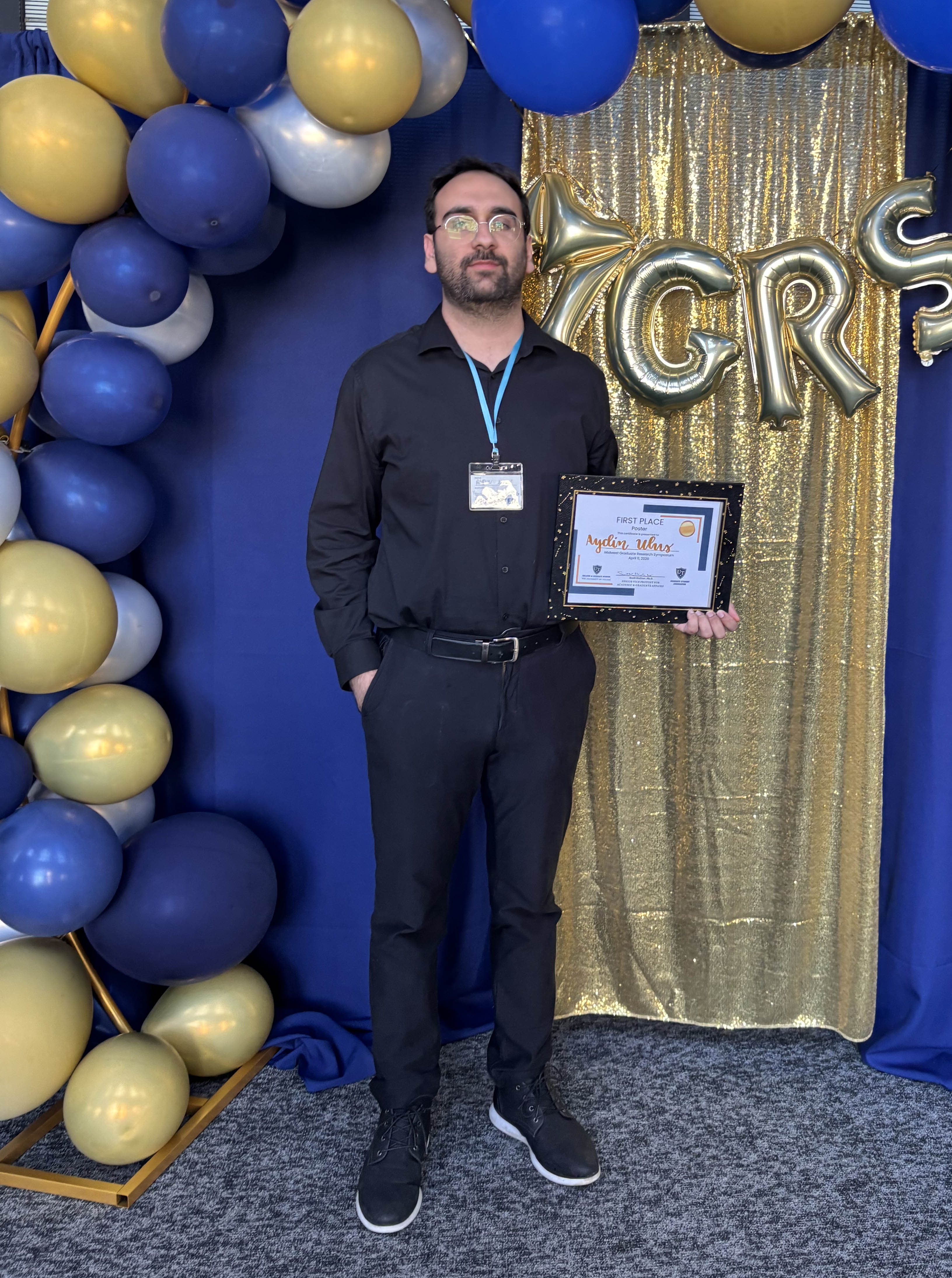Aydin Ulus posing with his first place certificate at the 2026 Midwest Graduate Research Symposium.