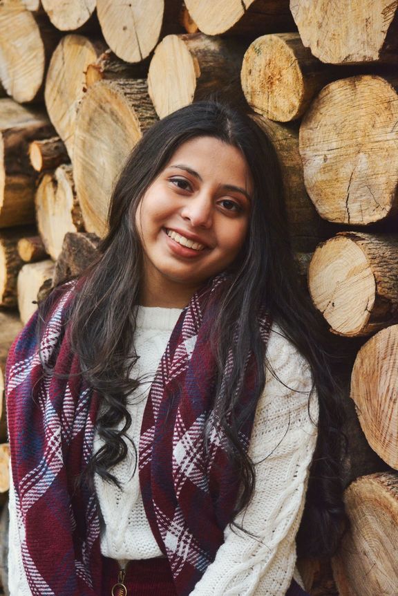 Photo of Nirmiti Shah smiling in front of wall of tree logs