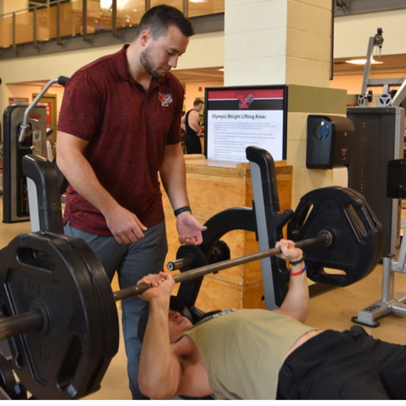 Personal Trainer assisting patron bench pressing weight bar and plates