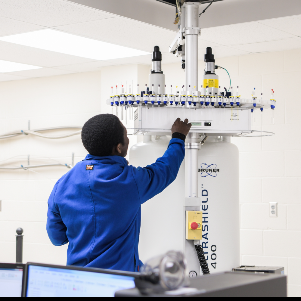 student in white lab coat operating lab machinery