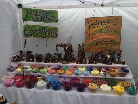 A photo of a vendor booth titled 'Mystic Creations' that has fairy sculpture, wax candles and tarts displayed