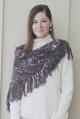 A woman with a tan turtleneck and handwoven purple and pink yarn scarf around her neck