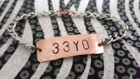 A bracelet with a gold-plated metal template that reads 33yo