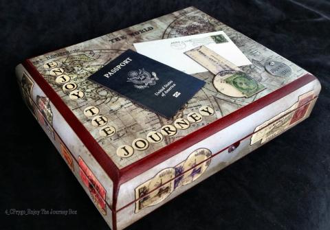 A box with a map of the world painted on the top with the words 'Enjoy the Journey' along the sides. A passport and envelope are glued to the top