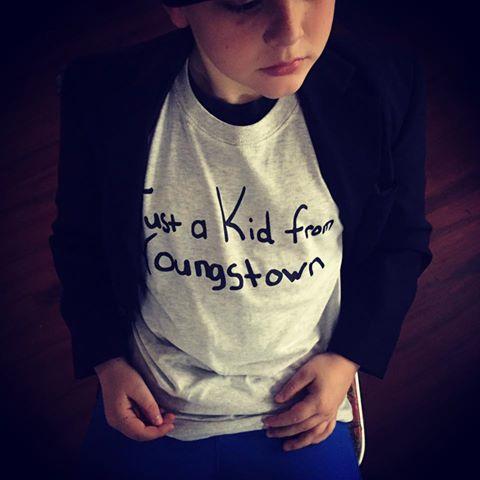 A young boy wearing a gray 'Just a kid from Youngstown' shirt
