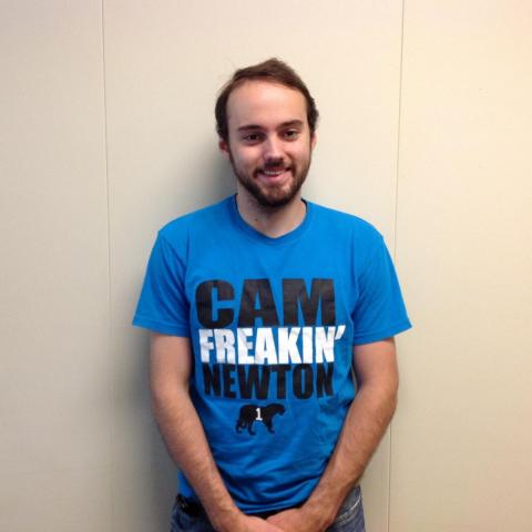 Male student wearing a blue t shirt that reads 'Cam Freakin' Netwon', posing against a white wall