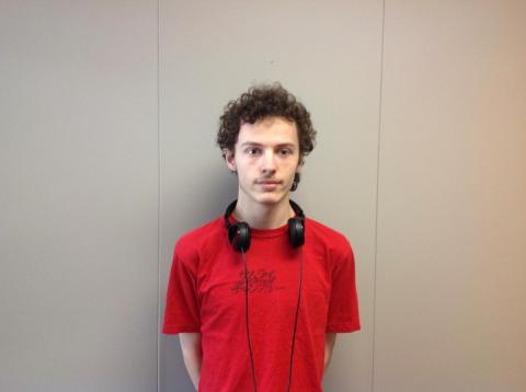 Male student wearing a red t shirt and headphones posing against a wall