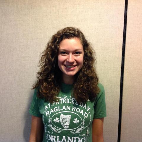 Smiling female student wearing a green t shirt posing against a wall