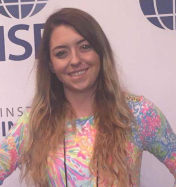A smiling female student in a multicolor dress posing against a wall at a convention