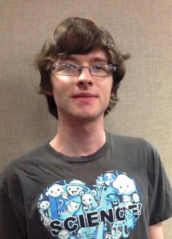 A male student slightly smiling at the camera, wearing glasses and a tshirt that says "heart science"