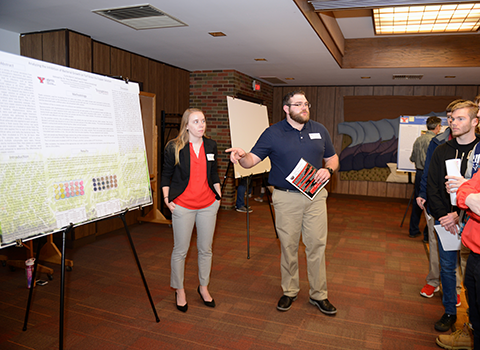 Two students explaining a poster to a group of people