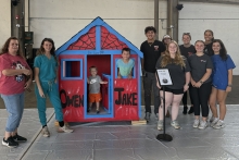 students and teaching assistants from YSU’s Sokolov Honors College standing next to the custom playhouse they built and decorated for Owen and Jake who are inside the playhouse