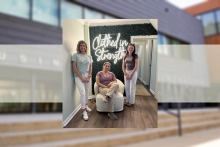 members of the Student Nonprofit Leadership Organization pose in front of the Clothed in Strength logo