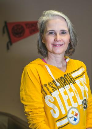 Gina McGranahan posing in her office wearing a yellow Pittsburgh Steelers sweatshirt